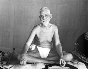 Photo of Ramana Maharshi on couch in old hall on tiger skin legs crossed in black and white